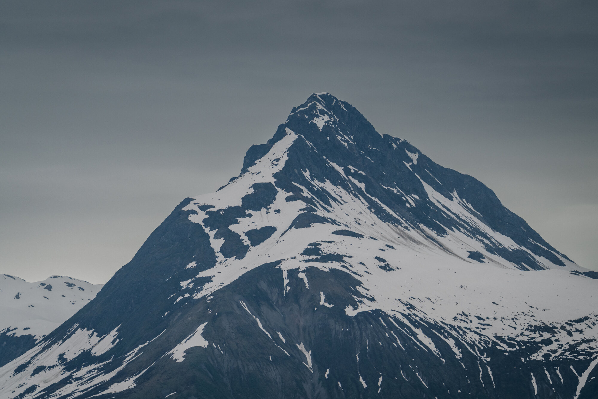 Dark steep Alaska mountain ribbed with snow and partly wrapped in low cloud