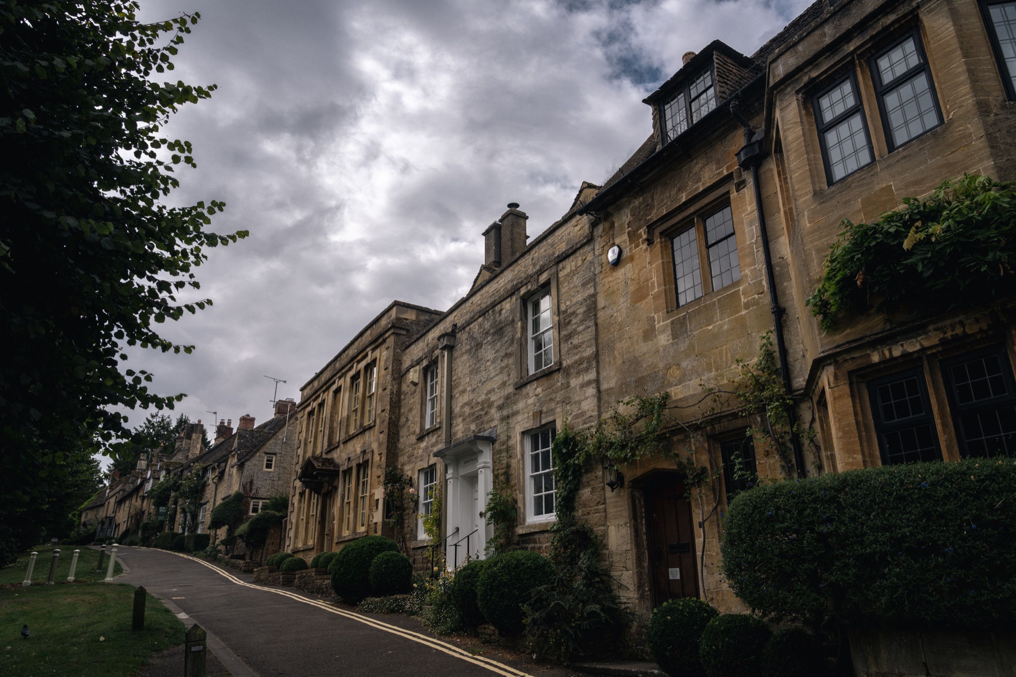 Row of historic Cotswold stone houses beneath a dramatic dark storm sky