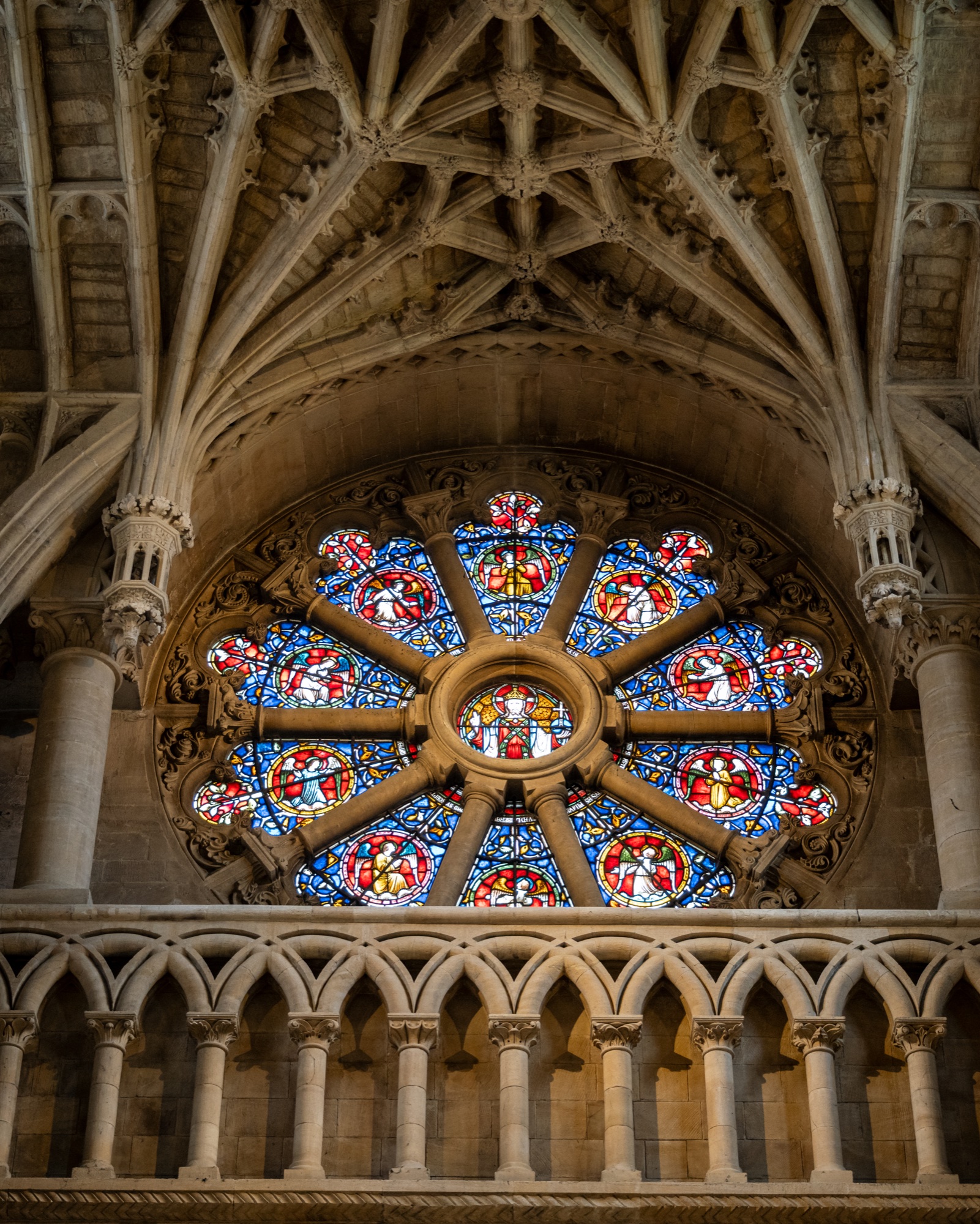 Colorful Oxford cathedral rose window framed by carved Gothic stone ribs and columns