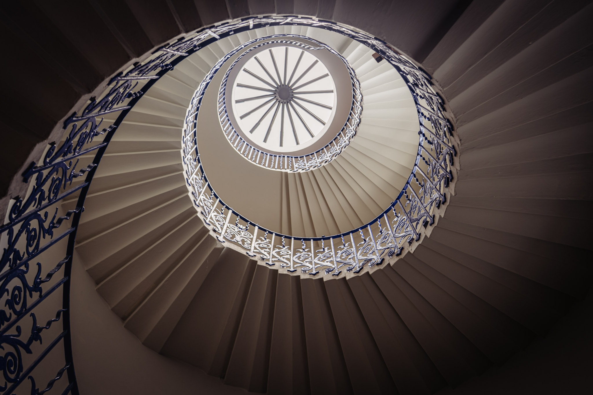 Tulip Stairs spiraling upward around blue wrought-iron railings toward a circular skylight at the Queen's House in Greenwich
