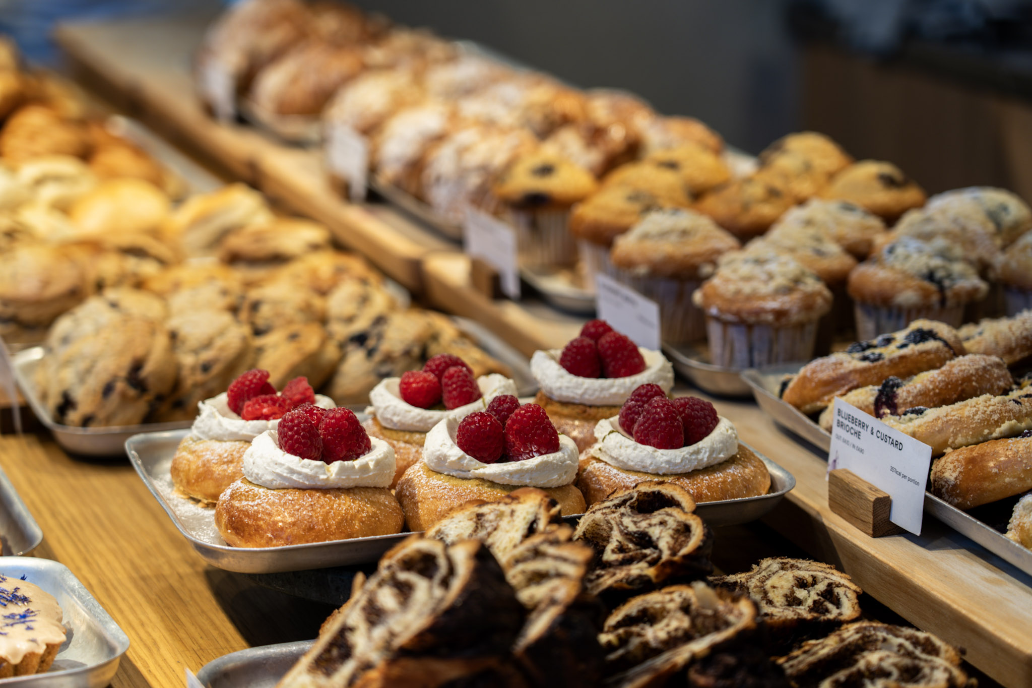 London bakery display filled with buns, pastries, muffins, and raspberry-topped brioche