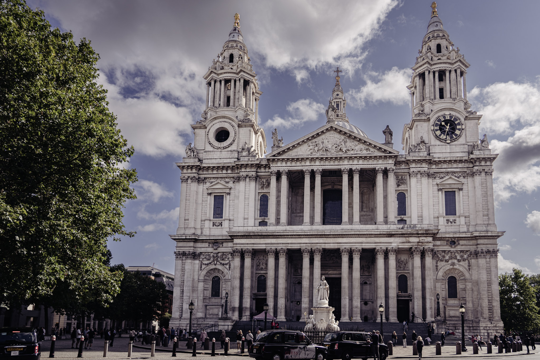 West front of St Paul's Cathedral framed by a leafy tree and dramatic broken clouds