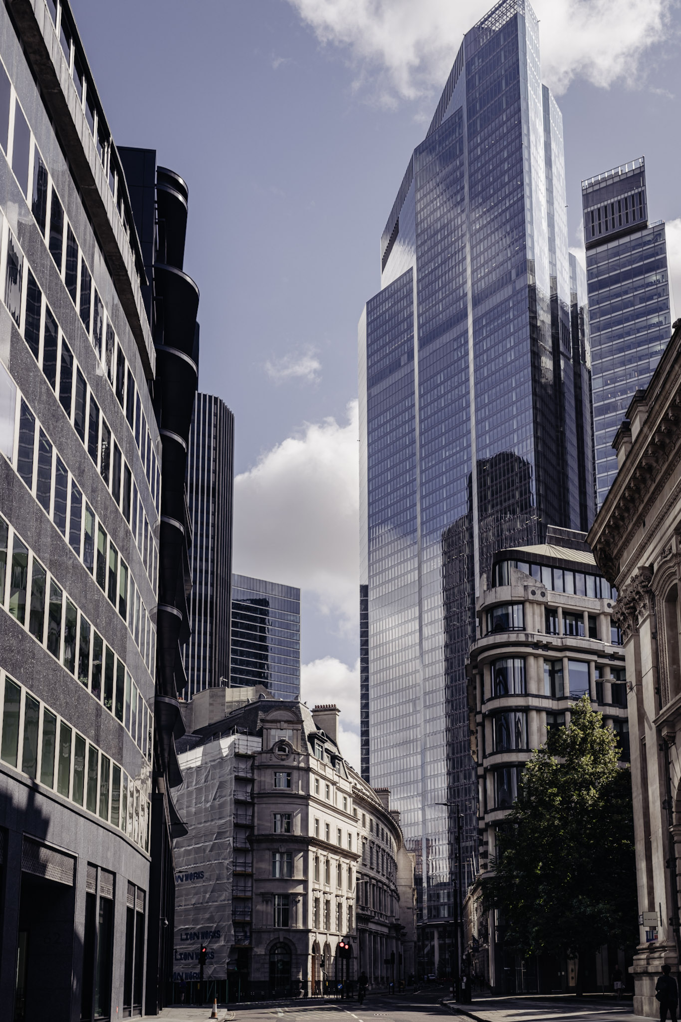8 Bishopsgate rising in stacked glass blocks through a narrow City of London street between older façades