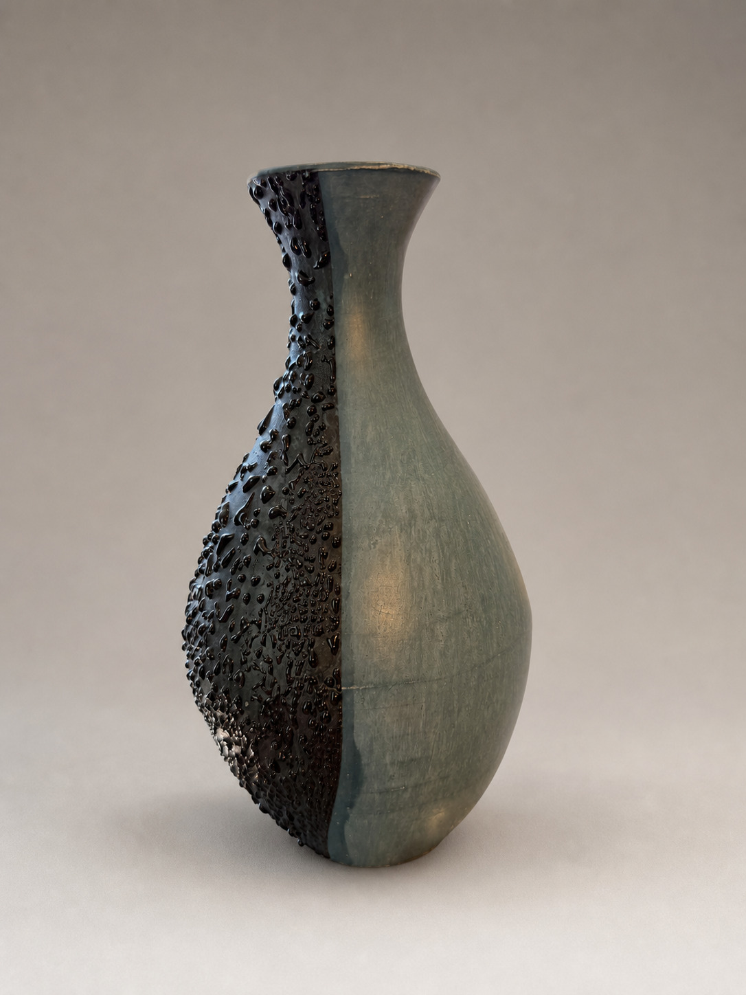 Side angle of a blue-green terra sigillata vase divided by a black textured surface