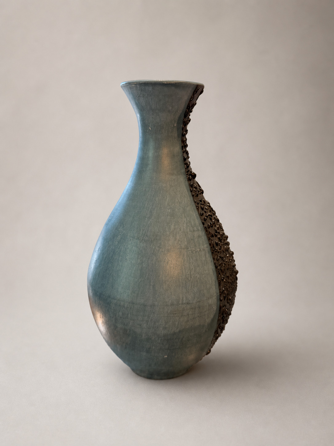 Three-quarter view of a blue-green terra sigillata vase with black texture appearing along one edge