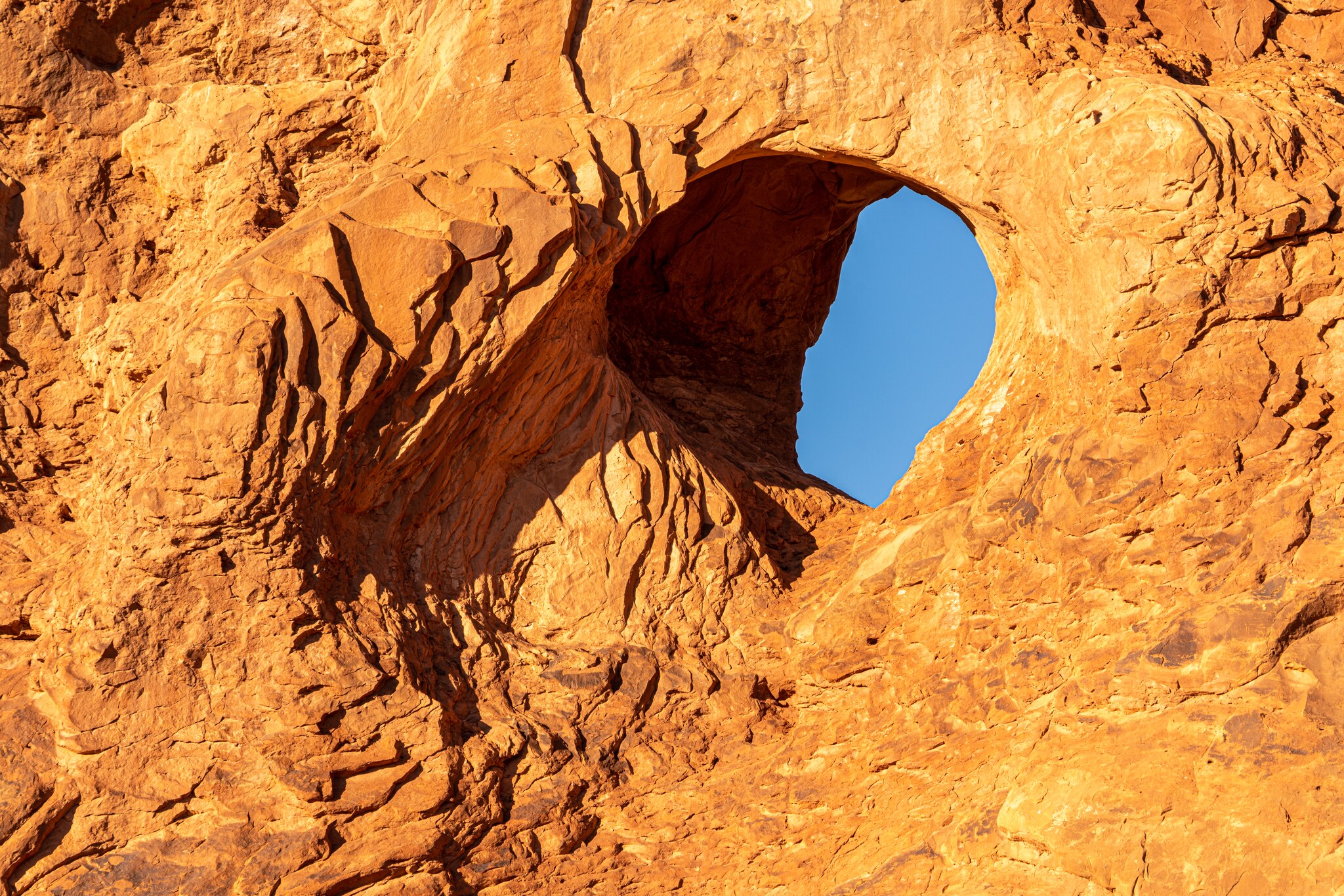 Small rounded opening in intensely textured golden sandstone revealing a patch of blue sky